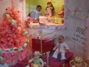 American Girl dolls in window display with pink Christmas tree